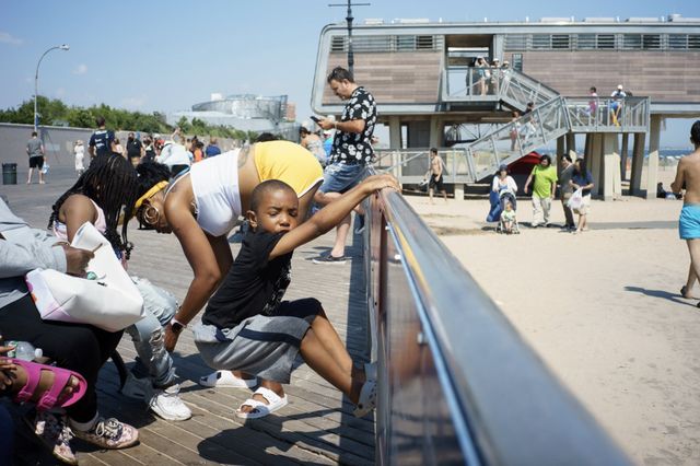 a child hangs on a railing on the Coney Island boardwalk